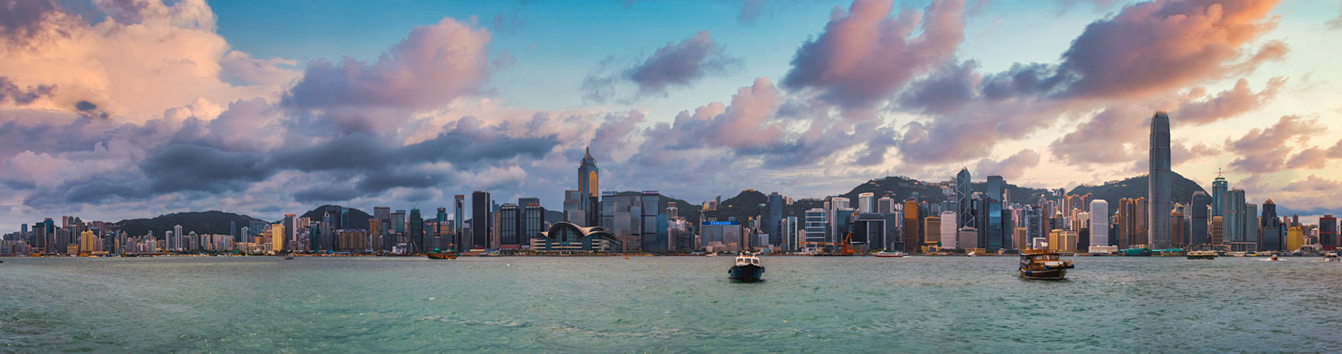 Victoria Harbour at first light, ferries crossing smooth dawn water, the Hong Kong skyline ranged behind under streaked cloud.