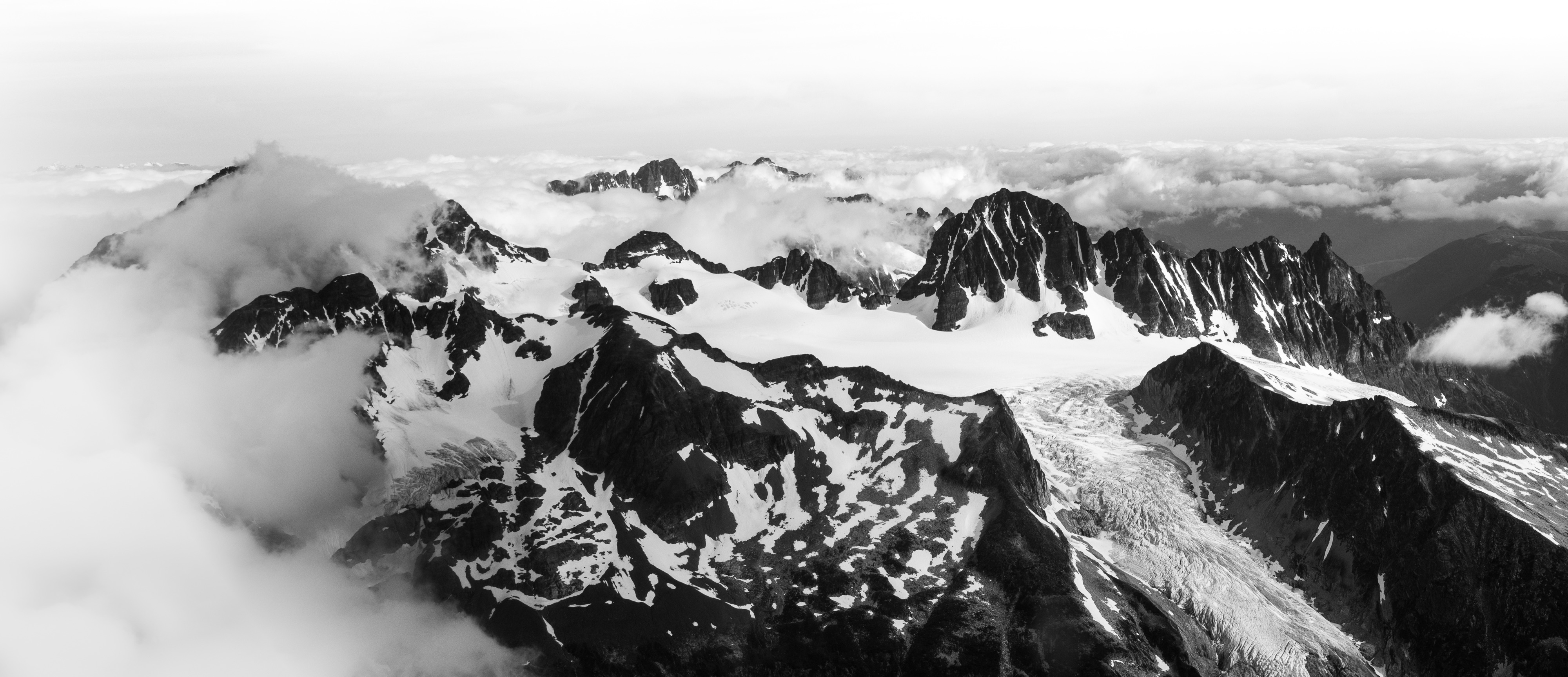 Black-and-white panorama of glaciated peaks rising through a sea of cloud.